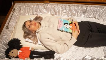 Elizabeth Pich liegt mit Comicbuch «Fungirl» und einer Spielpuppe im Sarg