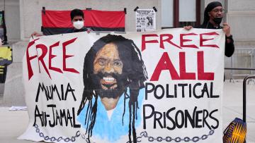 Aktivist:innen in Philadelphia mit einem Transparent mit der Aufschrift «Free Mumia Abu-Jamals – Free All Political Prisoners»