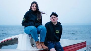 Sarah Mardini und Seán Binder sitzten auf einem kleinen Boot am Strand