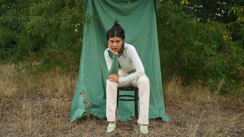 Şeyda Kurt sitzt im Freien auf einem Stuhl vor einem grünen Tuch