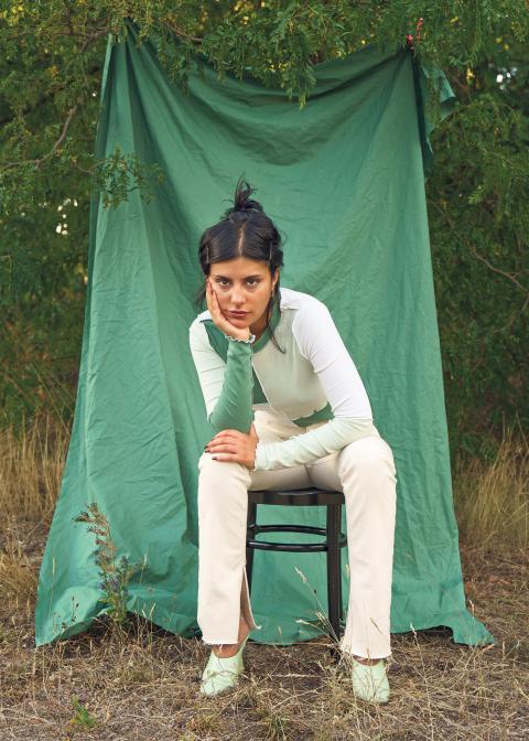 Şeyda Kurt sitzt im Freien auf einem Stuhl vor einem grünen Tuch