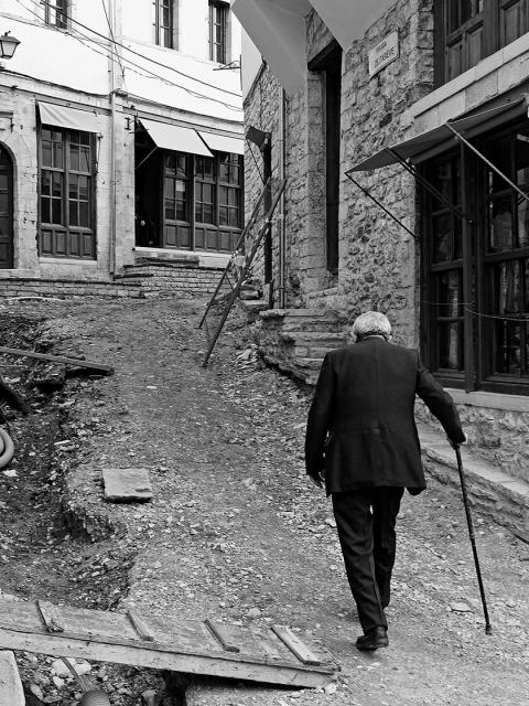 ein alter Mann mit Stock geht durch eine Gasse in Gjirokastra, Südalbanien