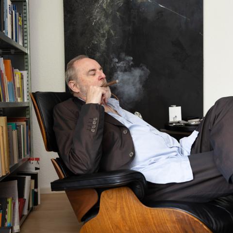 Peter Schneider sitzt auf einem Sessel und raucht Zigarre