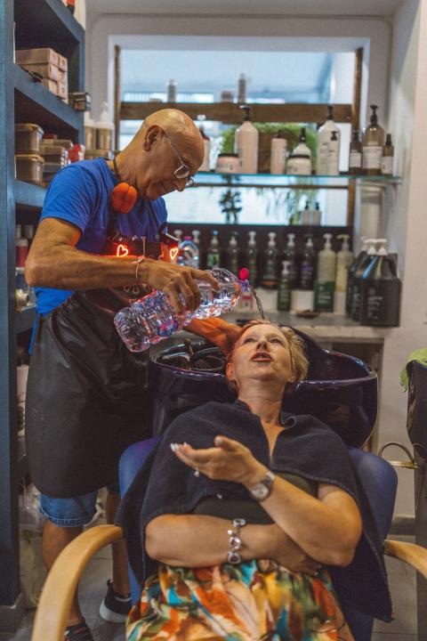 Coiffeur Enzo Schasta wäscht einer Kundin die Haare mit Wasser aus einer PET-Flasche