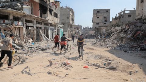 Menschen sind zu Fuss und mit dem Fahrrad zwischen zerstörten Gebäuden im Zentrum von Gaza-Stadt unterwegs