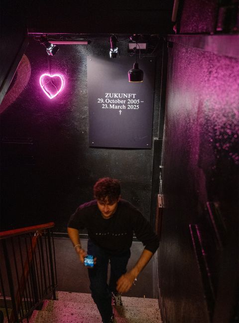 eine Person läuft die Treppe des Zürcher Club Zukunft hoch, im Hintergrund ein Plakat mit der Aufschrift «ZUKUNFT 29. October 2005 – 23. March 2025 †»