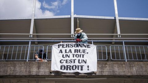 eine Person hängt ein Transparent mit der Aufschrift «PERSONNE A LA RUE, UN TOIT C'EST UN DROIT!» auf