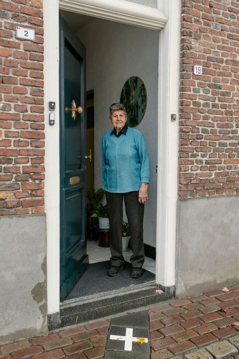 eine ältere Frau steht am Hauseingang eines Hauses in der Enklave H7, wo die Grenze direkt durch die Eingangstür verläuft