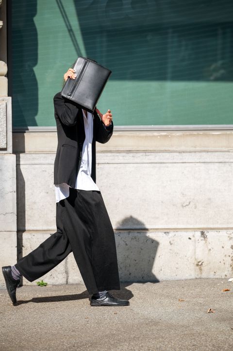 eine Person verdeckt ihr Gesicht mit einer Tasche