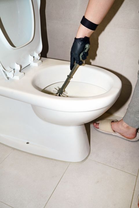 eine Person reinigt ein WC mit einer Toilettenbürste