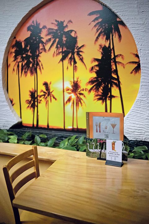 dekoratives Foto von Palmen an der Wand, im Vordergrund ein Restaurant-Tisch mit Speisekarte