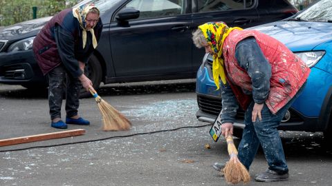 zwei ältere Frauen wischen Scherben bei Aufräumarbeiten in Kyjiw zusammen