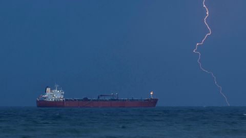 nächtliche Aufnahme eines Tankers vor dem Hafen von Muskat, im Hintergrund ist ein Gewitter-Blitz zu sehen