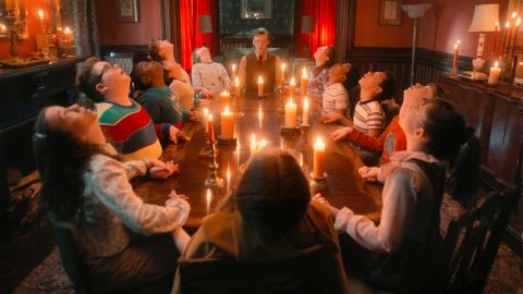 Videostill aus der TV-Serie «Stranger Things»: junge Personen sitzen an einem Tisch und halten sich die Hände und starren zur Decke