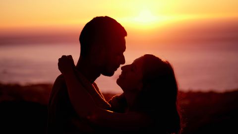 Symbolfoto: ein Paar küsst sich vor einem Sonnenuntergang