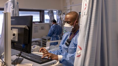 ein Pfleger mit Maske tippt sitzt vor einem Computer