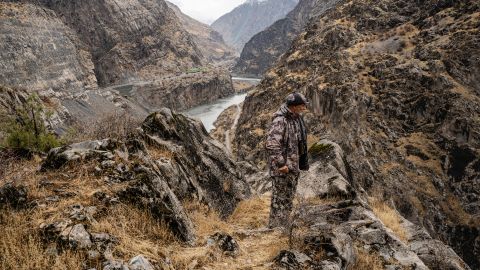 Dawlatchon Mullojorow blickt auf den Grenzfluss Pandsch, im Hintergrund ist eine Strasse in der Schlucht zu sehen
