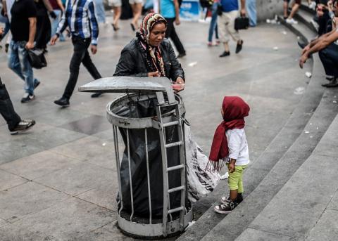 Frau aus Syrien und ihr Kind durchsuchen einen Abfallbehälter nach Essbarem