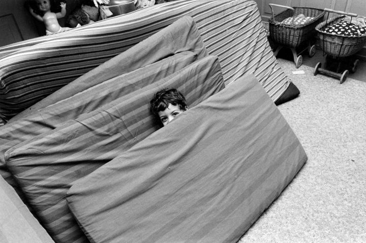 ein Kind versteckt sich hinter einer Matratze