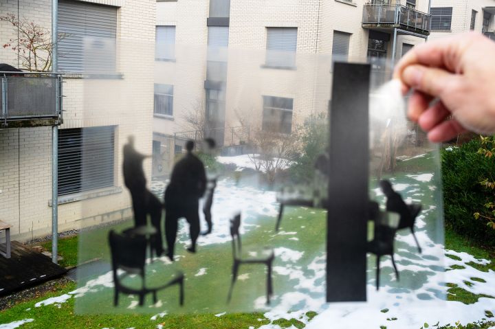 Fotografie einer Folie die Menschen zeigt, die auf Stühlen sitzen und daneben stehen, im Hintergrund ein Gebäude in St. Gallen