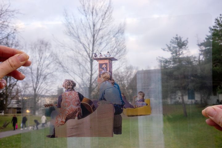 Fotografie einer Folie, auf der Menschen zu sehen sind, welche auf Sofas sitzen, im Hintergrund eine Wiese