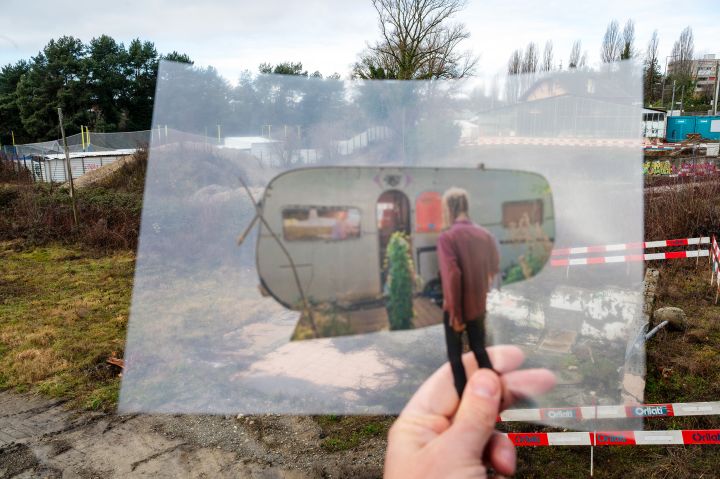 Fotografie einer Folie, auf der eine Person vor einem Wohnwagen zu sehen ist, im Hintergrund eine Baustelle