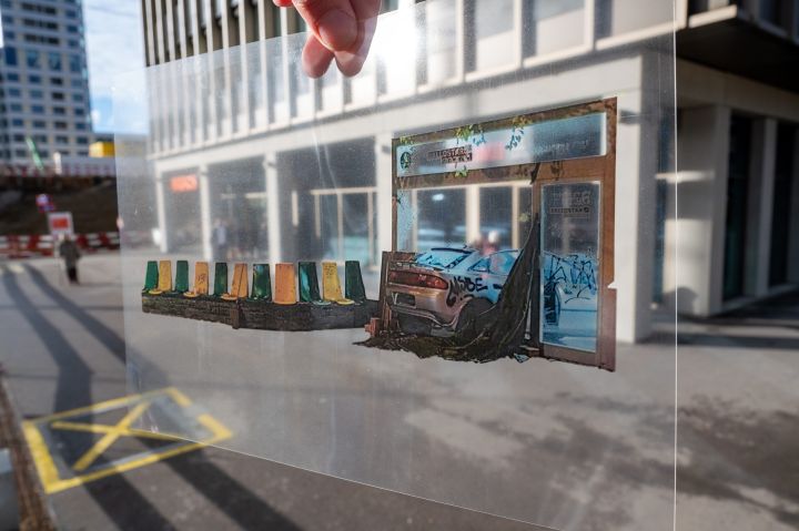 Fotografie einer Folie, auf der Stühle und ein bespraytes Auto zu sehen sind, im Hintergrund ein modernes Gebäude