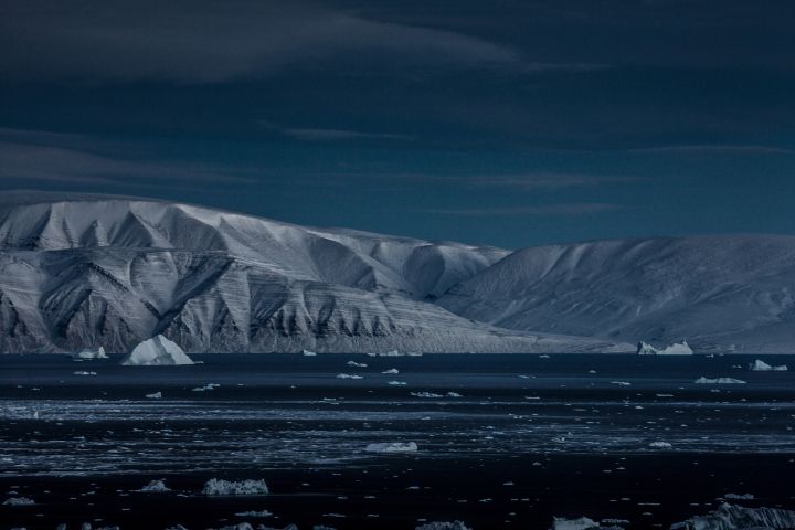 Nachtaufnahme von Eisschollen im Wasser und dahinter Küstengebiet