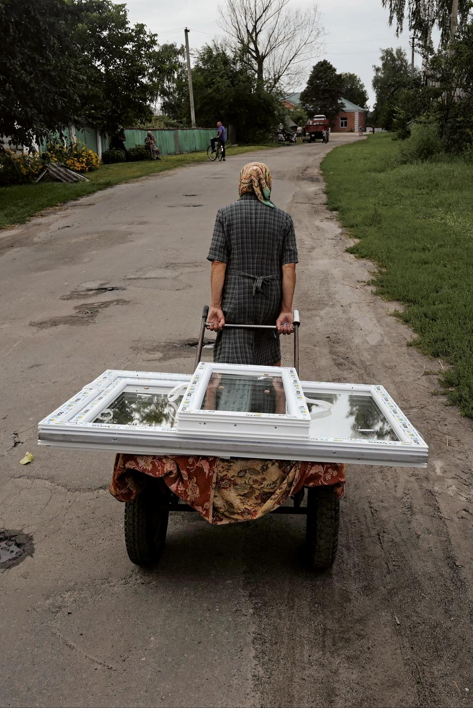 Eine Frau bringt neue Fenster zu ihrem teilweise zerstörten Haus, Region Tschernihiw, August 2022.
