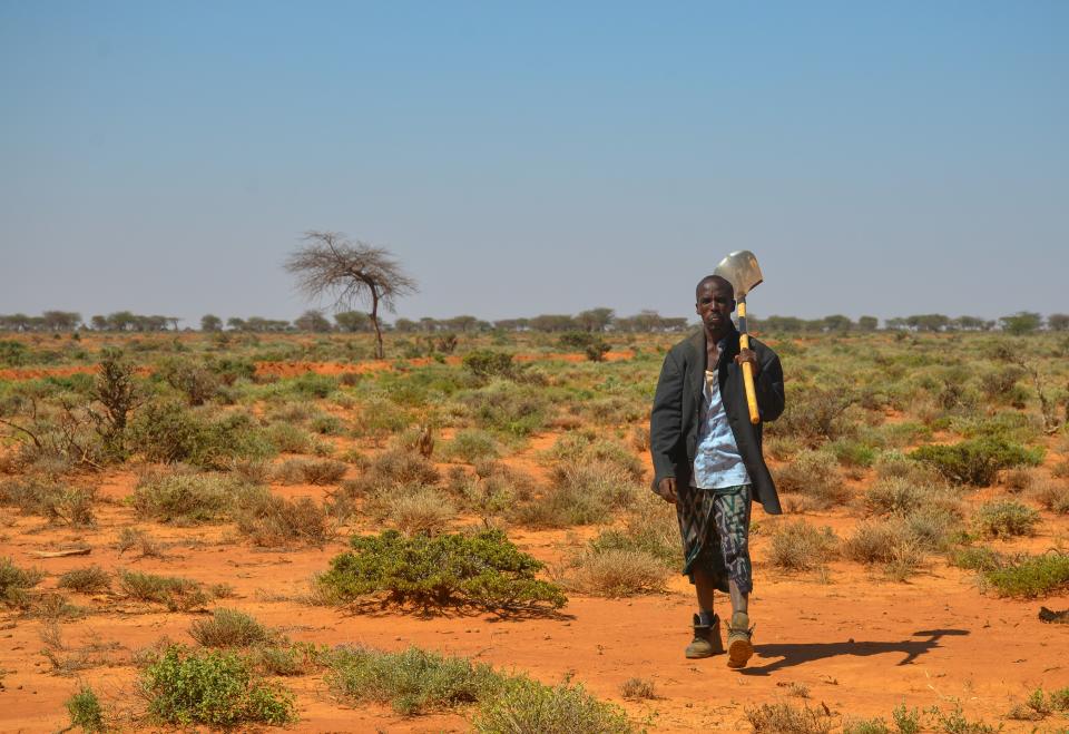 Abdirisak Mohamed Hussien schreitet mit einer Schaufel auf der Schulter durch die Steppe