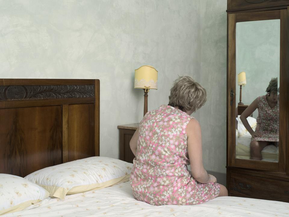 Selbstportrait-Inszenierung von Nora Rupp: Sie sitzt als alte Frau im Blumenkleid auf einem Bett