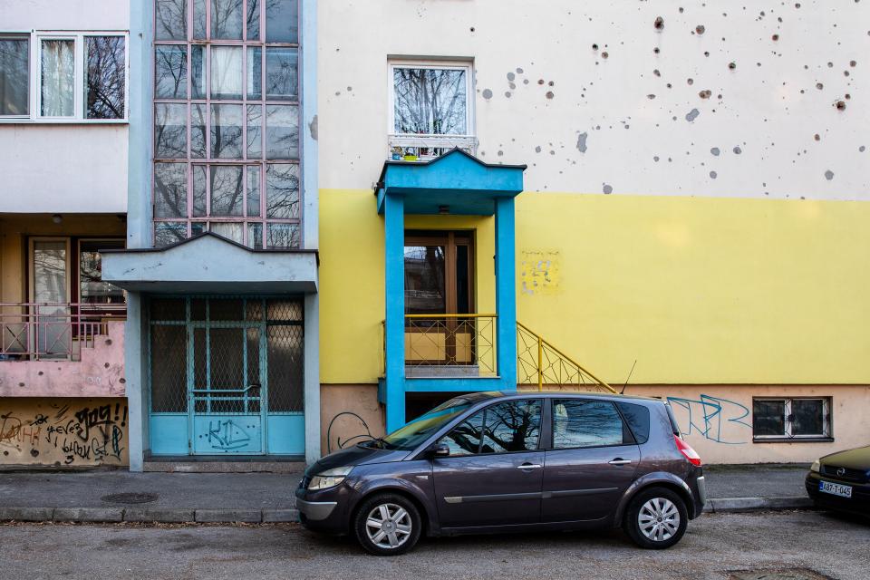Gebäude in Tuzla mit Einschusslöchern, im Vordergrund ein Auto