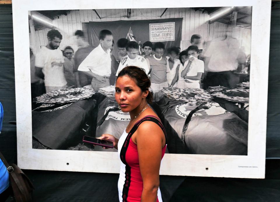 eine Frau steht vor einem Grossformat-Poster des Fotografen Sebastião Salgado, welcher die Beerdigung der Opfer des Massakers fotografiert hat