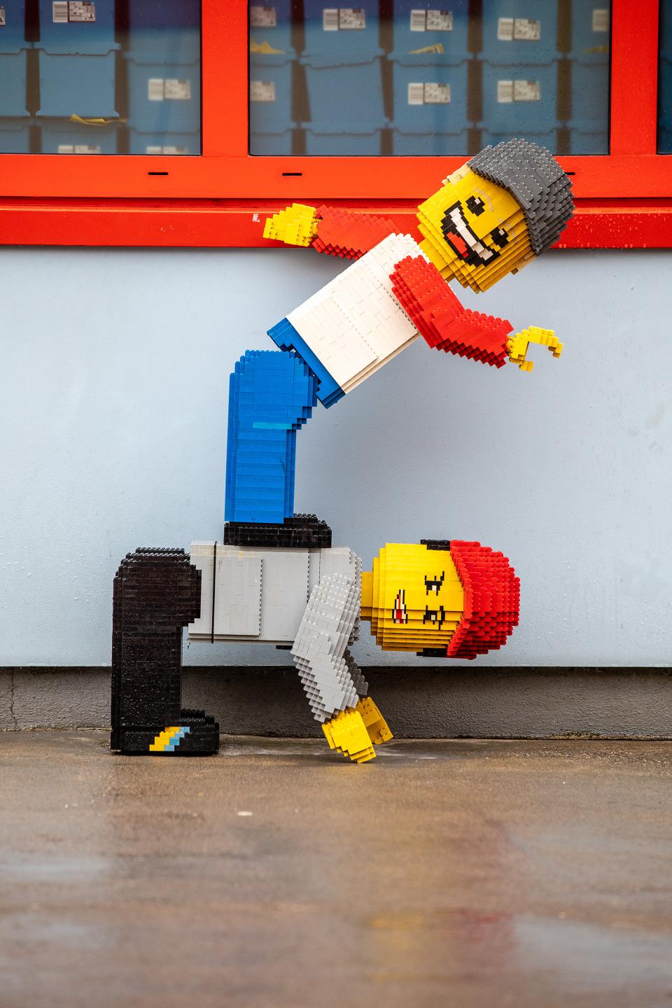 ein lebensgrosses Legomännchen, welches auf dem Rücken eines zweiten Legomännchen steht