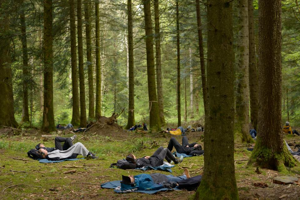 Besucher:innen des Waldtheaters liegen auf dem Waldboden und hören mit Kopfhörern einer Soundcollage von Rimini Protokoll zu