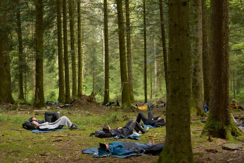 Besucher:innen des Waldtheaters liegen auf dem Waldboden und hören mit Kopfhörern einer Soundcollage von Rimini Protokoll zu 