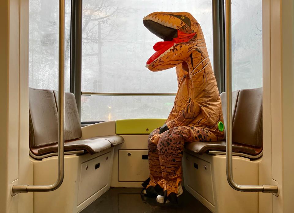 eine Person, welche als Dinosaurier verkleidet ist, sitzt im Tram