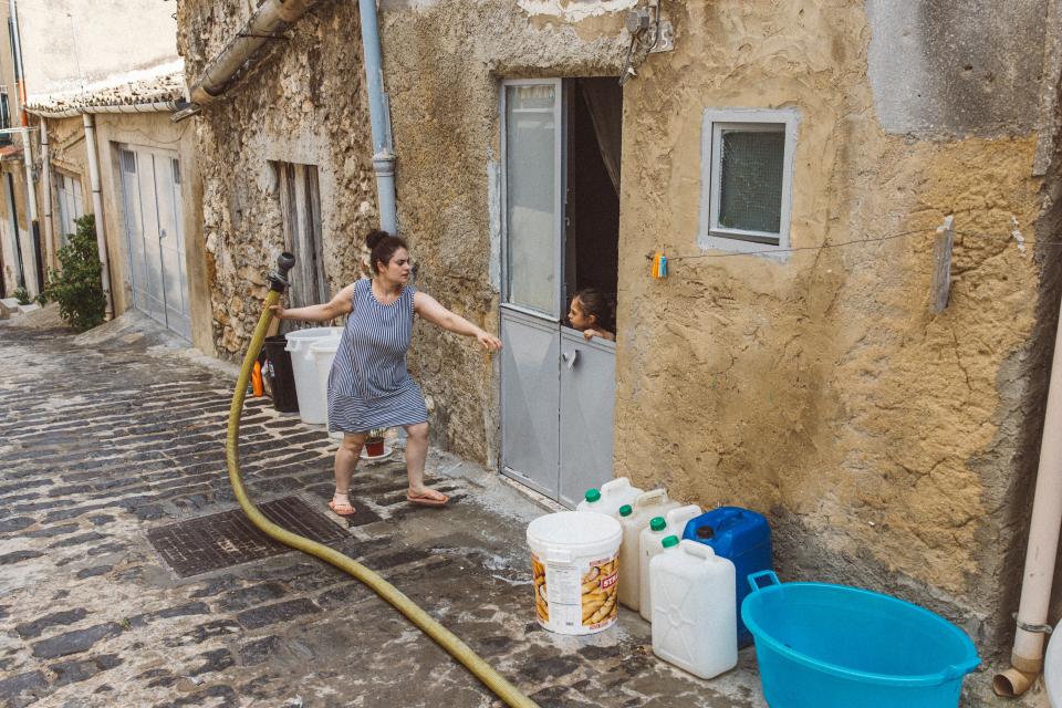 eine Frau füllt vor ihrem Haus Kübel und Kanister mit Wasser ab