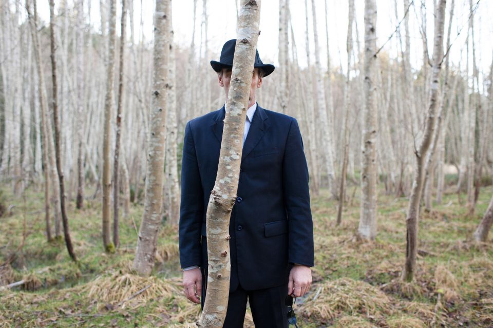 Symbolbild: ein Mann steht hinter einem Baum im Wald
