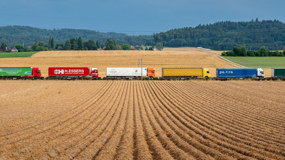 Symbolbild: Lastwagen auf einem Güterzug, welcher in ländlicher Gegend unterwegs ist