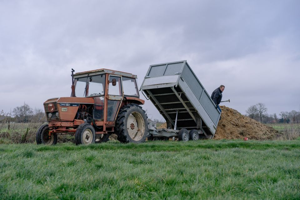 ein Mann lädt mit Traktor und Anhänger den Mist seiner Pferde als Dünger auf einem Acker ab