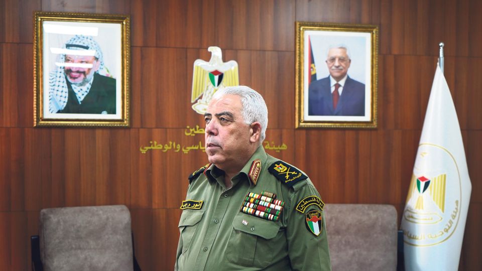 Anwar Radschab steht in einem Büro mit Portraits von Jassir Arafat und Mahmud Abbas an der Wand 