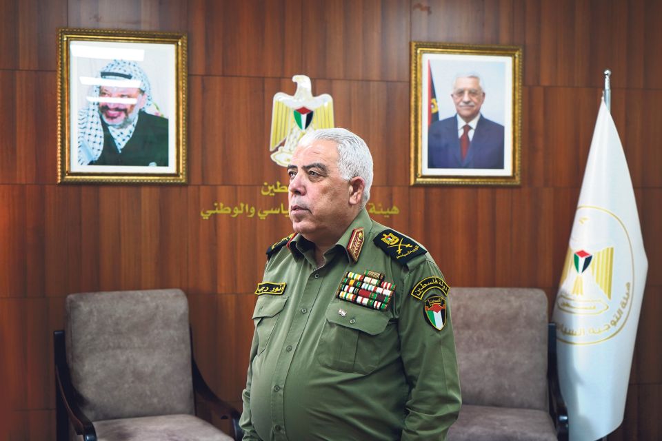 Anwar Radschab steht in einem Büro mit Portraits von Jassir Arafat und Mahmud Abbas an der Wand 