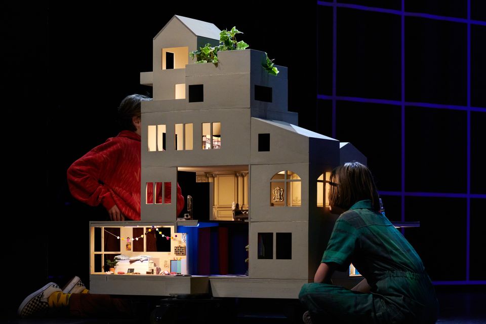 Bühnenfoto des Theaterstück «Die Zauberformel von Zürich»: zwei Personen schauen in ein Puppenhaus