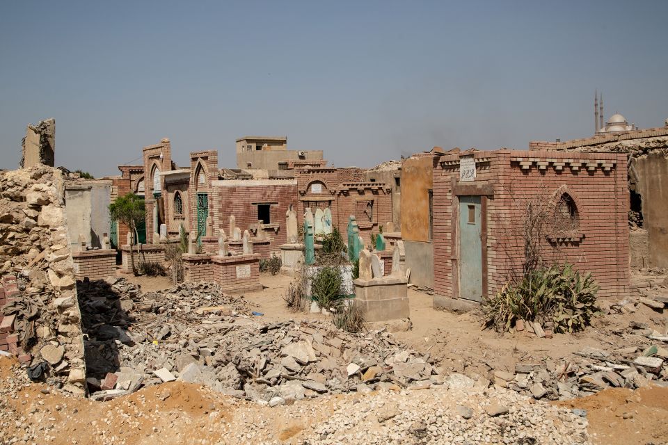 zerstörte Gruft in der Stadt der Toten, im Hintergrund ein Wohnhaus und eine Moschee