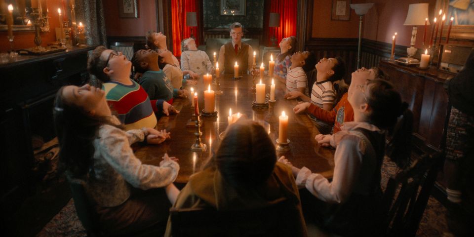 Videostill aus der TV-Serie «Stranger Things»: junge Personen sitzen an einem Tisch und halten sich die Hände und starren zur Decke