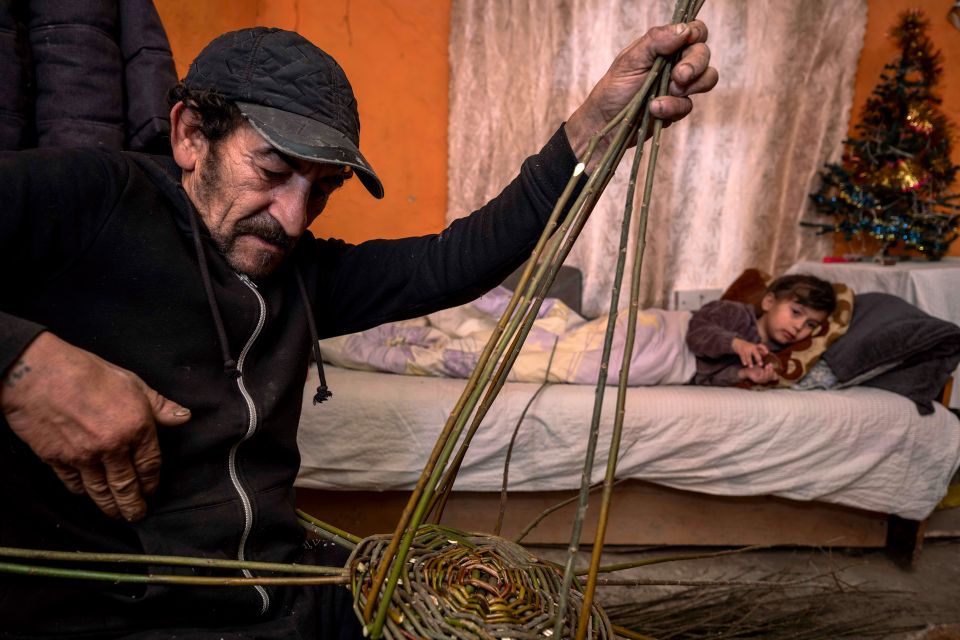 Ferenc Lakatos flechet einen Korb, im Hintergrund liegt ein Kind auf einem Bett