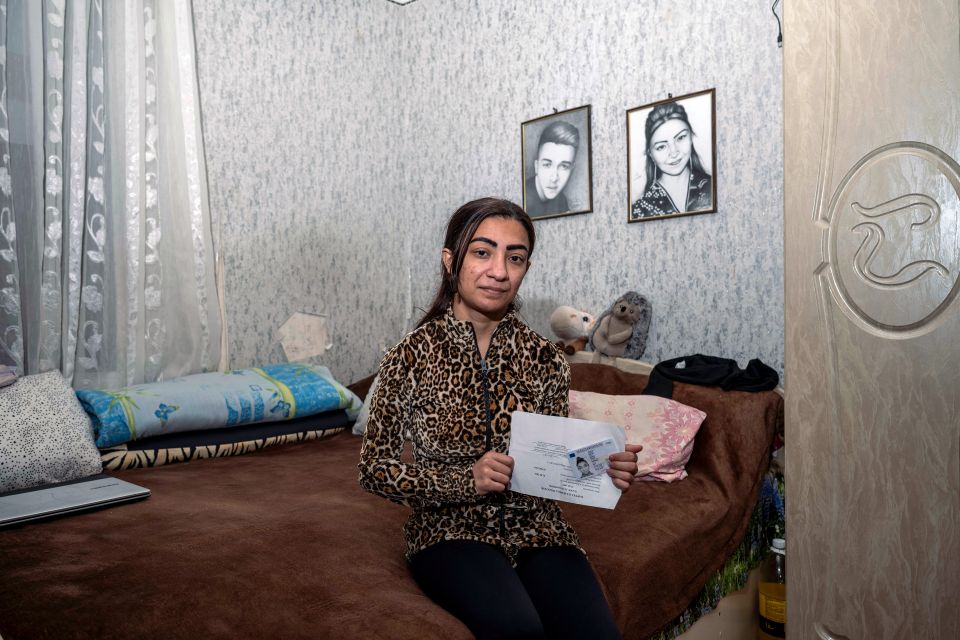 Diana Balog sitzt auf einem Bett und zeigt ihre Geburtsurkunde