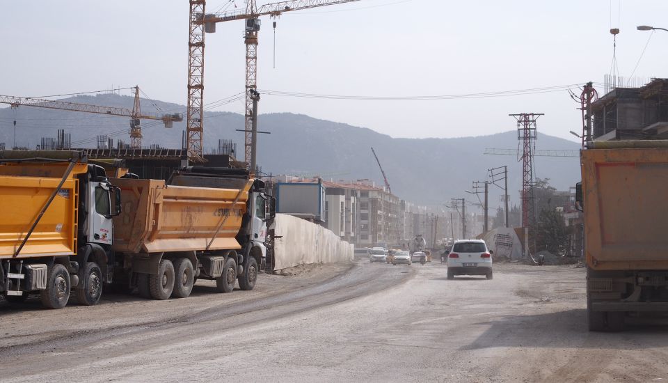 Lastwagen und Baukräne entlang einer staubigen Strasse in Antakya