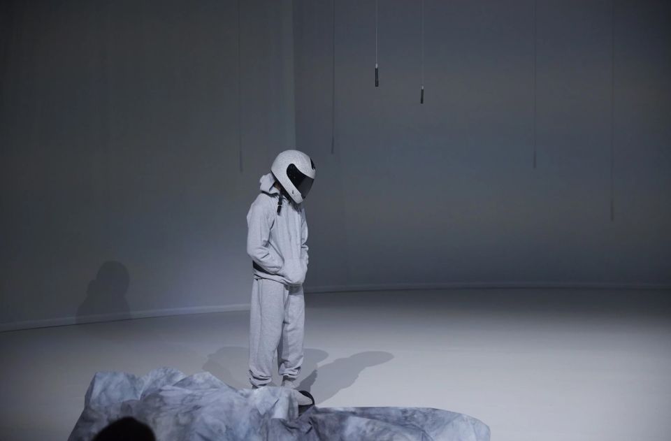 Bühnenfoto der Tanzproduktion «from rock to rock»: eine Person im Trainingsanzug und Helm steht auf der Bühne